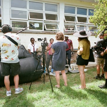 Film crew hold industrial film equipment outdoors in Barbados.