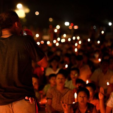 A man speaks on a loudspeaker to a gathered crowd who are holding lit candles, some holding their hands up in solidarity