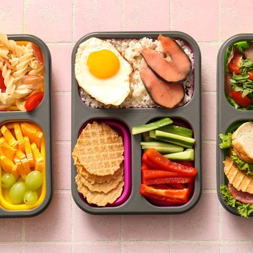 Lunchboxes with different tasty food on pink tile background