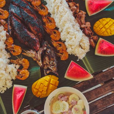A table with banana leaves and cooked shrimp, fish and rice laid out on top